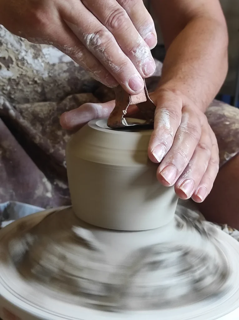 Manos usando una herramienta de madera para recortar una pieza de cerámica en el torno