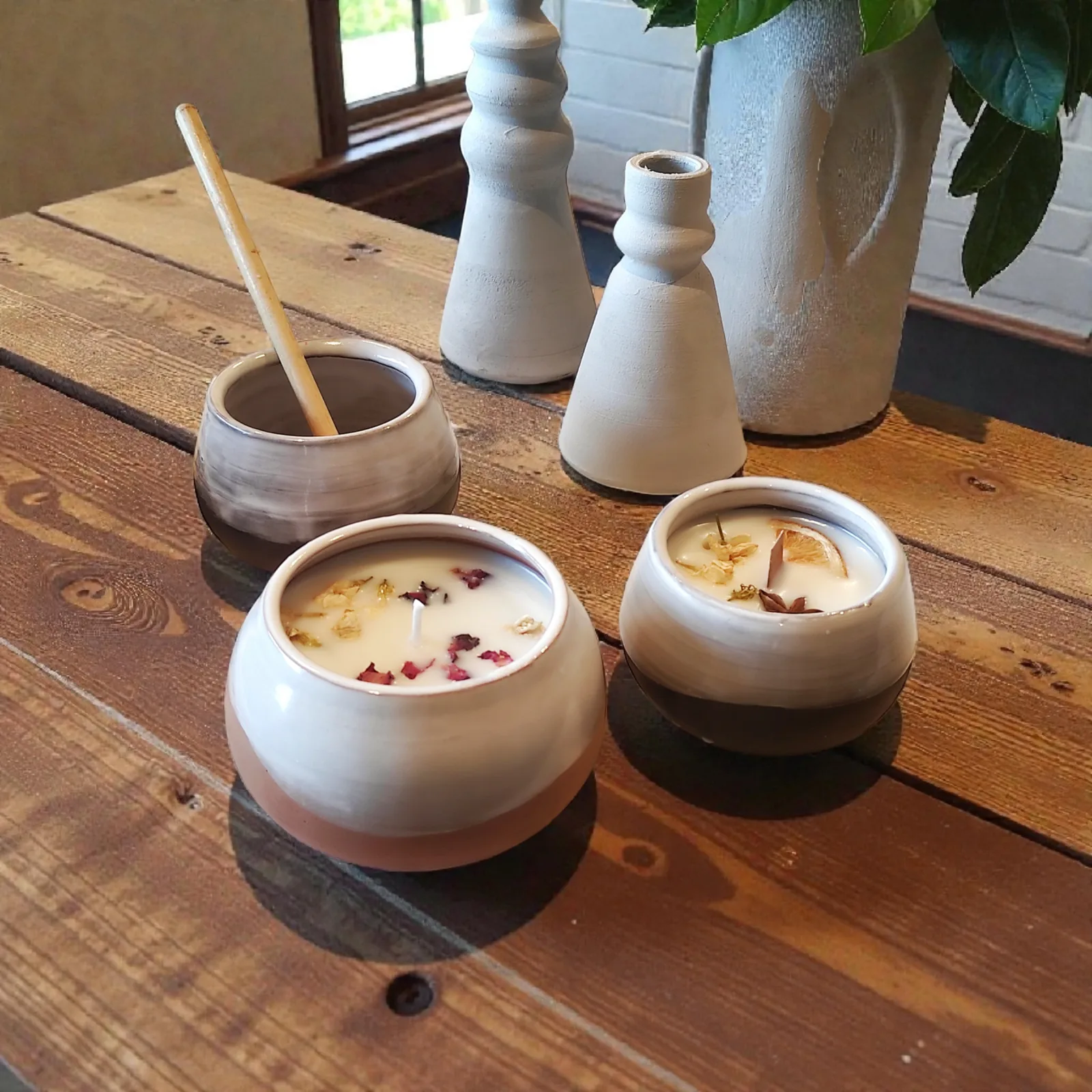 Velas aromáticas en cuencos de cerámica bicolor y jarrones blancos sobre mesa de madera